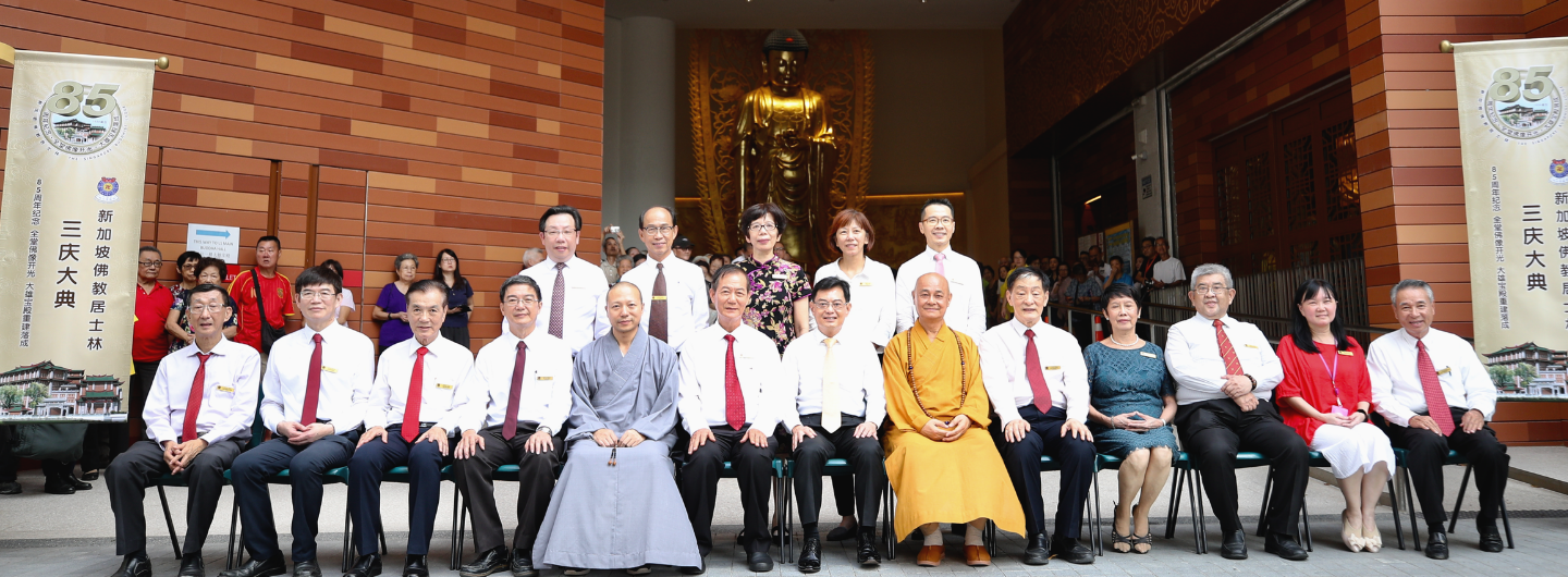 Group of people seated in front of a golden Buddha statue and a banner.